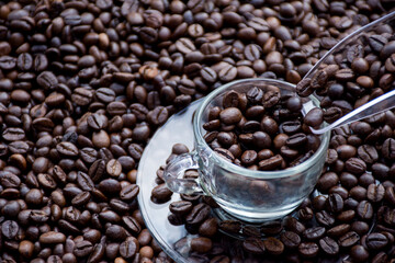 a glass spoon filling up a glass cup with coffee beans, surrounded by coffee beans
