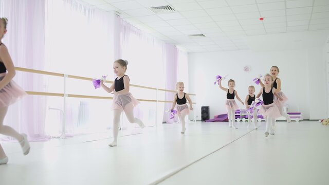 Little girls with toys in hands are runing in ballet classroom