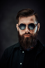 Closeup portrait of a cool bearded male in sunglasses on a dark background