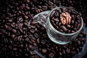 Coffee cup with saucer filled and surrounded by black coffee beans and a walnut inside the cup on top of the beans