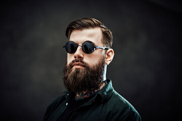 Obraz premium Closeup portrait of a cool bearded male in sunglasses on a dark background