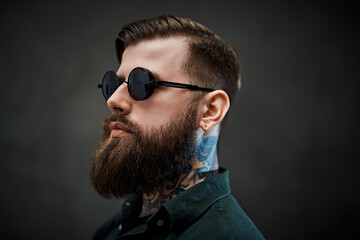 Closeup portrait of a cool bearded male in sunglasses on a dark background