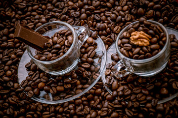 Fototapeta premium Coffee cups with saucers surrounded and filled with coffee beans, one with a chocolate bar and the other with a walnut