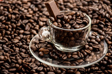 Coffee cup with saucer surrounded and filled up with coffee beans and chocolate inside the cup