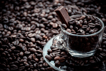 Coffee cup with saucer surrounded and filled up with coffee beans and chocolate inside the cup