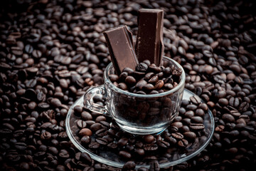Coffee cup with saucer surrounded and filled up with coffee beans and chocolate inside the cup