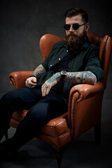 Cool bearded young man sitting on a vintage chair in a dark studio