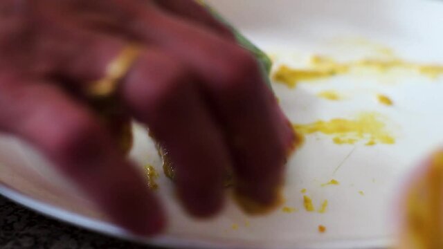 Indian woman coating an arvi arbi leaf with marinate of flour and spices on a white plate to make a popular indian dish of pakode and bhajiye for frying