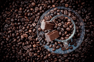 Coffee cup with saucer surrounded and filled up with coffee beans and chocolate inside the cup
