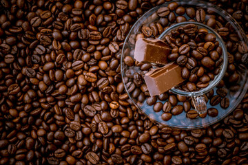 Coffee cup with saucer surrounded and filled up with coffee beans and chocolate inside the cup