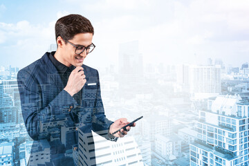 Young handsome businessman in suit and glasses using phone and thinking how to tackle the problem, new career opportunities, MBA. Bangkok on background. Double exposure.