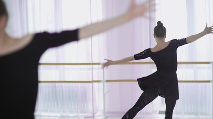 Young ballet dancer dancing on the background of a large window.