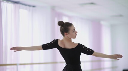 A professional ballerina in a black pack dances in a large training hall © stanis88
