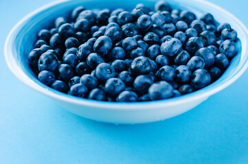 Blueberries in a bowl on a wooden table. Top view of plate and blueberries on violet surface