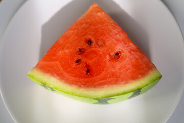 Close-Up Of Watermelon Slice on white plate Against White Background, with sunlight and shadow