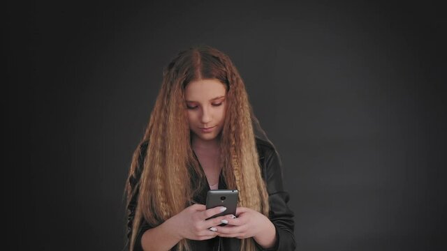 Internet communication. Social media. Teen girl creating message on smartphone isolated on dark background.