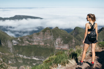 Athletic girl with  backpack in a sports uniform stands with his back to the frame against the backdrop of mountains and clouds. Mountain trekking
