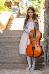 beautiful girl in a dress with a cello stands on the steps