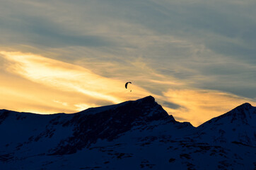 paraglider on a vibrant and bright dawn sky flying over majestic snow covered mountain top in the arctic circle