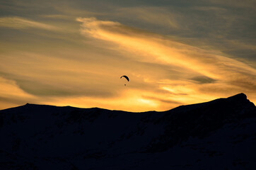 Obraz na płótnie Canvas Paraglider on vibrant colourful dawn sky with majestic snow covered mountain underneath in the arctic circle