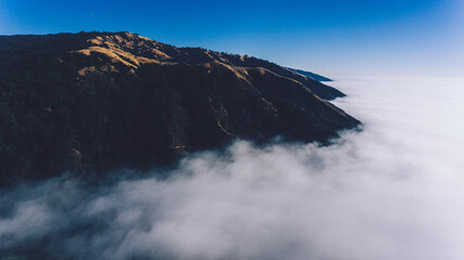 Aerial scenery view of rocky mountains covered with fog. Bird's eye view through clouds of mountainous terrain on high altitude