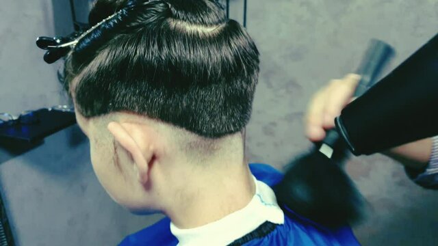 She cleans her hair with a brush and hair dryer after she finishes her haircut at the barber shop