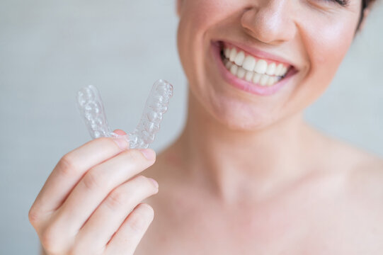 Close-up of orthodontic silicone transparent teeth aligner in female hands. A woman with a perfect charm smile holds a removable night retainer. Bracket for teeth whitening. Cropped photo.