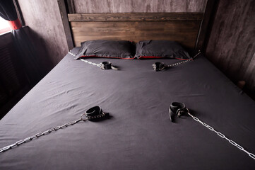 Bedroom for intimate meetings. VDSM equipment and sex toys. Leather handcuffs with a chain on a gray sheet. Fifty shades of gray. Fetish domination.