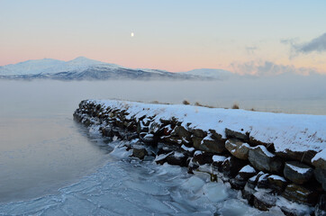 dense ice fog over frozen fjord with old rock pier and full moon