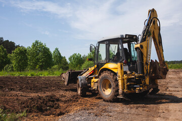 Clearing and leveling a private land plot. Yellow excavator driven earth in a wide bucket, back view