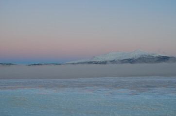 pink sunset sky in winter over frozen fjord and dense ice fog