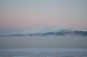 pink sunset sky in winter over frozen fjord and dense ice fog