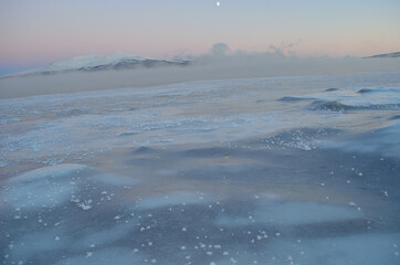 pink sunset sky and full moon over winter fjord with dense ice fog and reflection on water surface