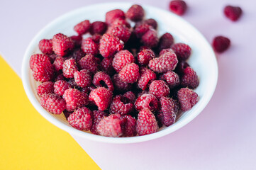 a beautiful light blue bowl of fruit with raspberries, blueberries and blackberries on yellow background, top view, studio shot
