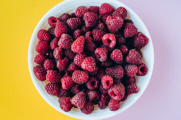 a beautiful light blue bowl of fruit with raspberries, blueberries and blackberries on yellow background, top view, studio shot