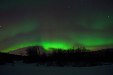 magnificent aurora borealis over frozen river bed and snowy mountain in the cold arctic circle night