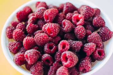 a beautiful light blue bowl of fruit with raspberries, blueberries and blackberries on yellow background, top view, studio shot
