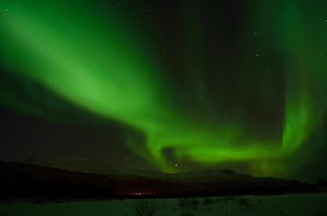 incredible strong aurora borealis over snowy mountain and frozen river bed in winter landscape