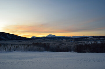 Fototapeta premium Scenic snowy mountain with vibrant colourful sky and white frost covered forest in the front