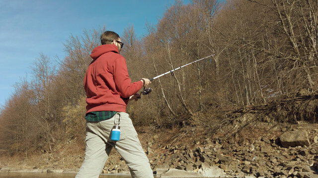 Adult man fishing at mountain stream. Throws a fishing rod into the river at the rocky terrain. Rolling the reel with fishing line.