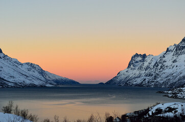 Colourful dawn sky over fjord with mighty snow covered mountains on each side in winter in arctic circle, northern Norway