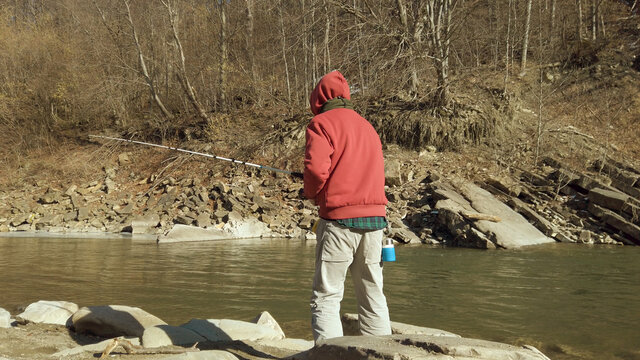 Adult man fishing at mountain stream. Throws a fishing rod into the river at the rocky terrain. Rolling the reel with fishing line.