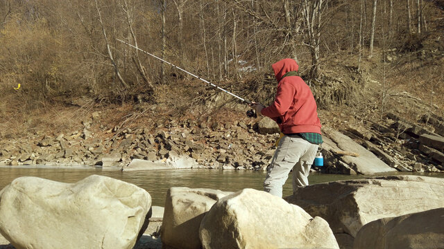 Adult man fishing at mountain stream. Throws a fishing rod into the river at the rocky terrain. Rolling the reel with fishing line.