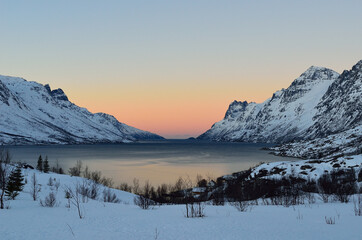 Colourful dawn sky over fjord with mighty snow covered mountains on each side in winter in arctic circle, northern Norway