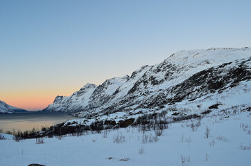 Naklejka premium High snow covered mountain surround fjord with vibrant dawn sky in the winter