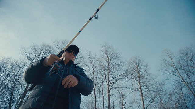 Adult man fishing at mountain stream. Throws a fishing rod into the river at the rocky terrain. Rolling the reel with fishing line.