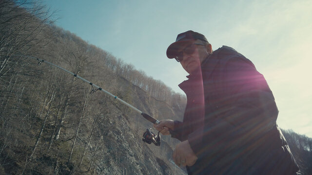 Adult man fishing at mountain stream. Throws a fishing rod into the river at the rocky terrain. Rolling the reel with fishing line.