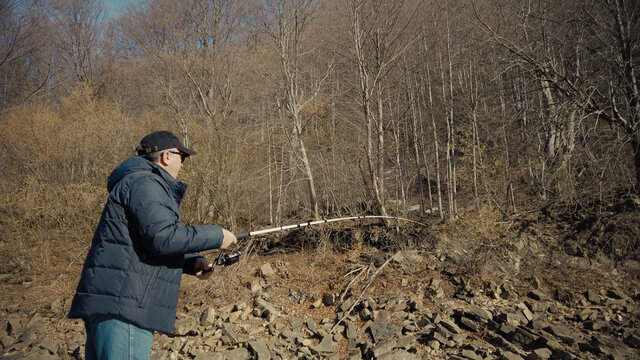 Adult man fishing at mountain stream. Throws a fishing rod into the river at the rocky terrain. Rolling the reel with fishing line.