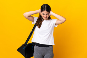 Young sport woman with sport bag isolated on yellow background frustrated and covering ears