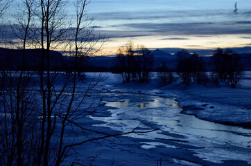 frozen river stream, snowt field and mighty mountain during the winter blue hour in northern Norway
